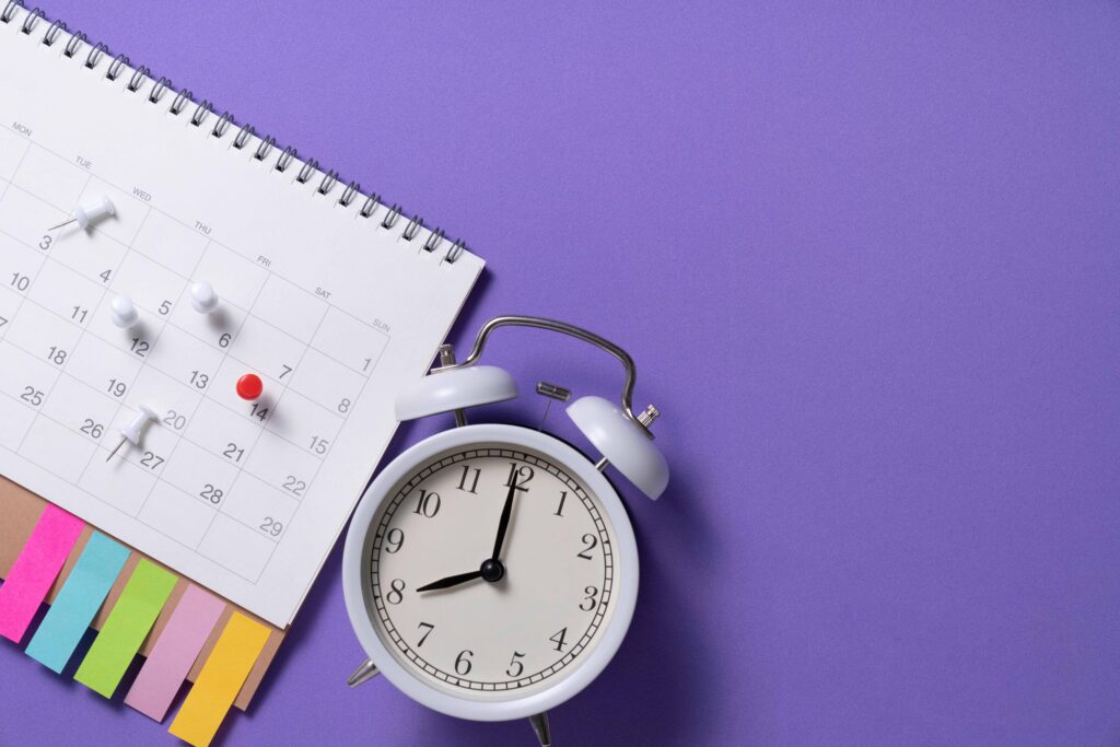 紫の背景の前にカレンダーと目覚まし時計が置かれている